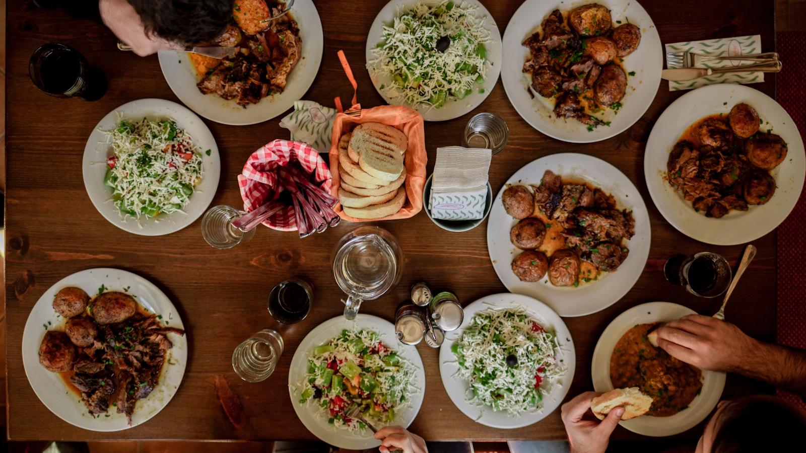 Mesa de refeição vista de cima, com vários pratos e pessoas à volta