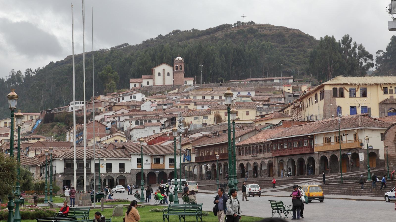 Praça de uma cidade colonial andina, com casario, igreja no alto e pessoas caminhando