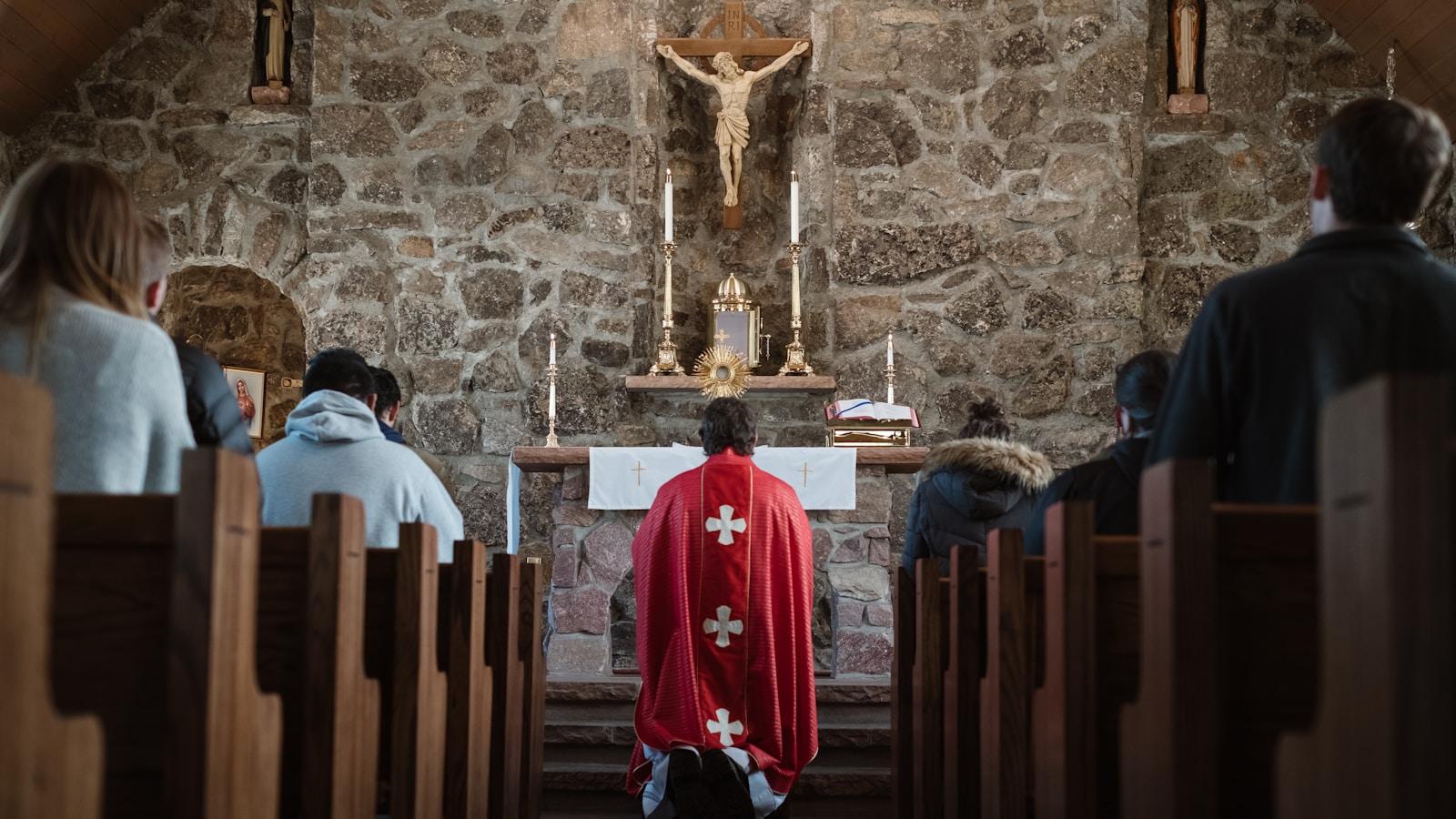 Sacerdote de casula vermelha diante do altar numa capela de pedra, visto do meio dos fiéis