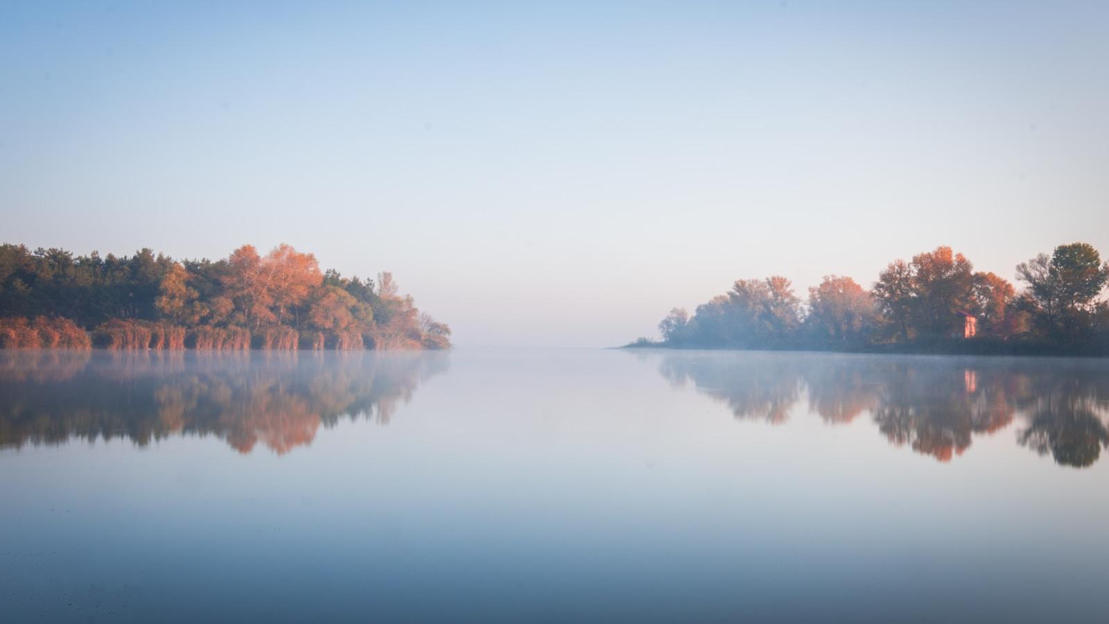 Lago calmo com névoa e árvores de outono refletidas na água