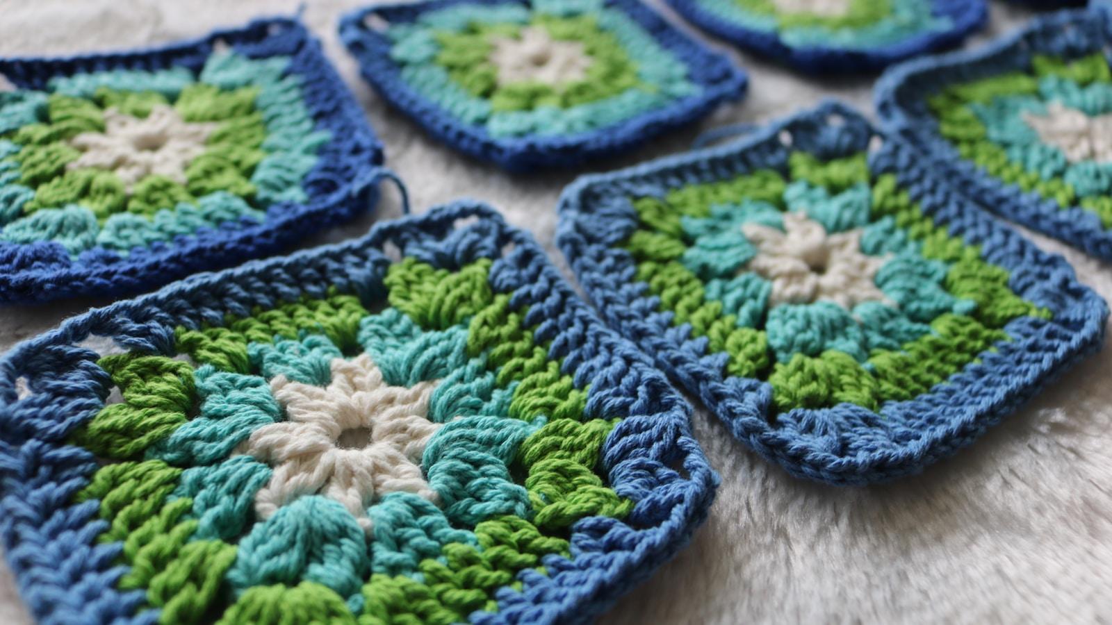 Quadrados de crochê em azul, verde e branco sobre uma superfície clara