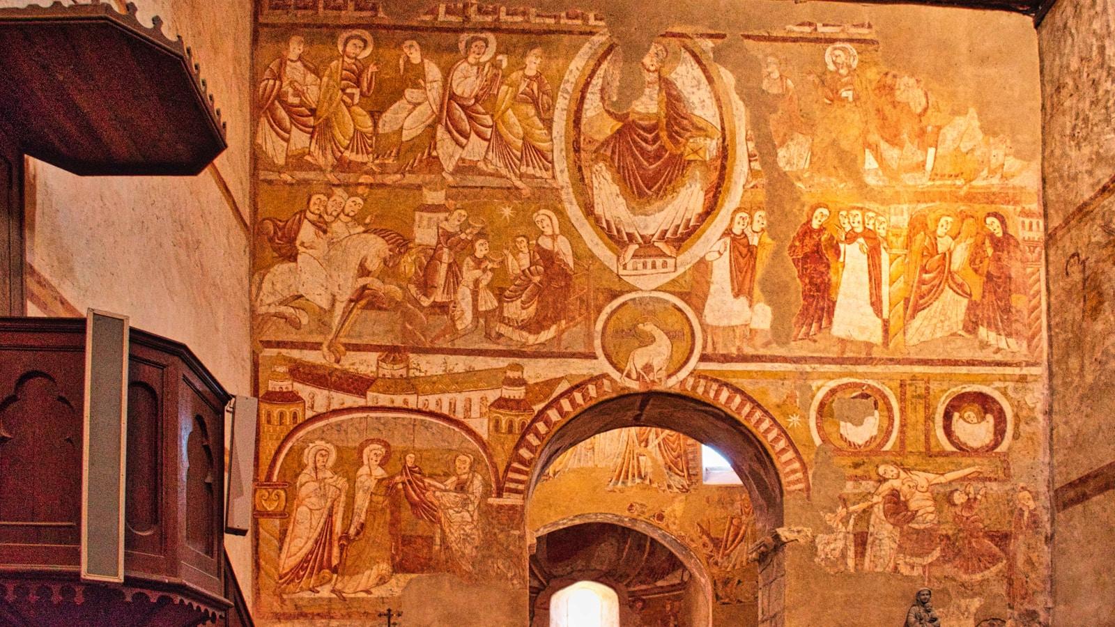 Parede de igreja antiga coberta de afrescos medievais, com um púlpito de madeira