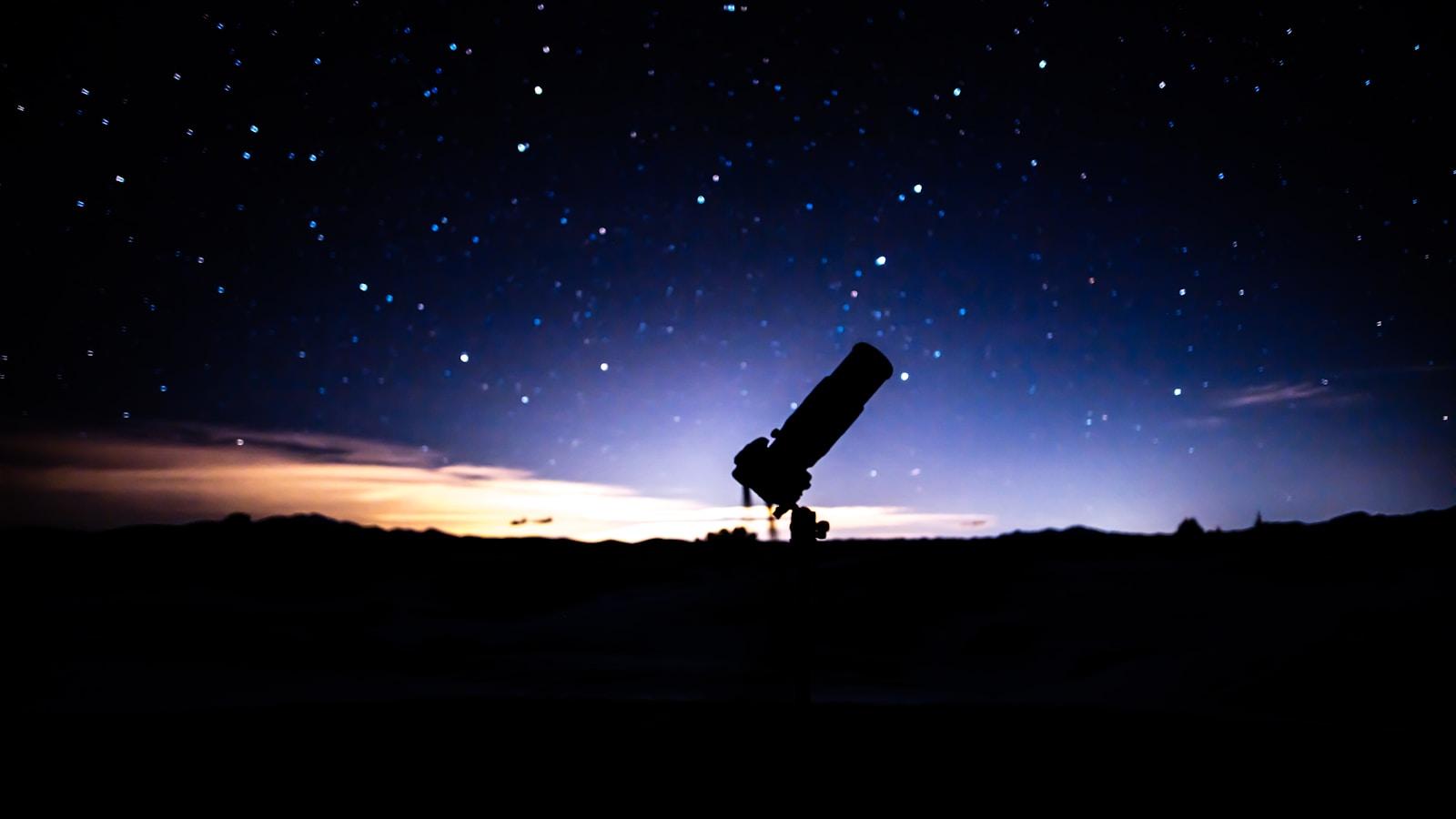 Silhueta de um telescópio contra o céu estrelado ao anoitecer