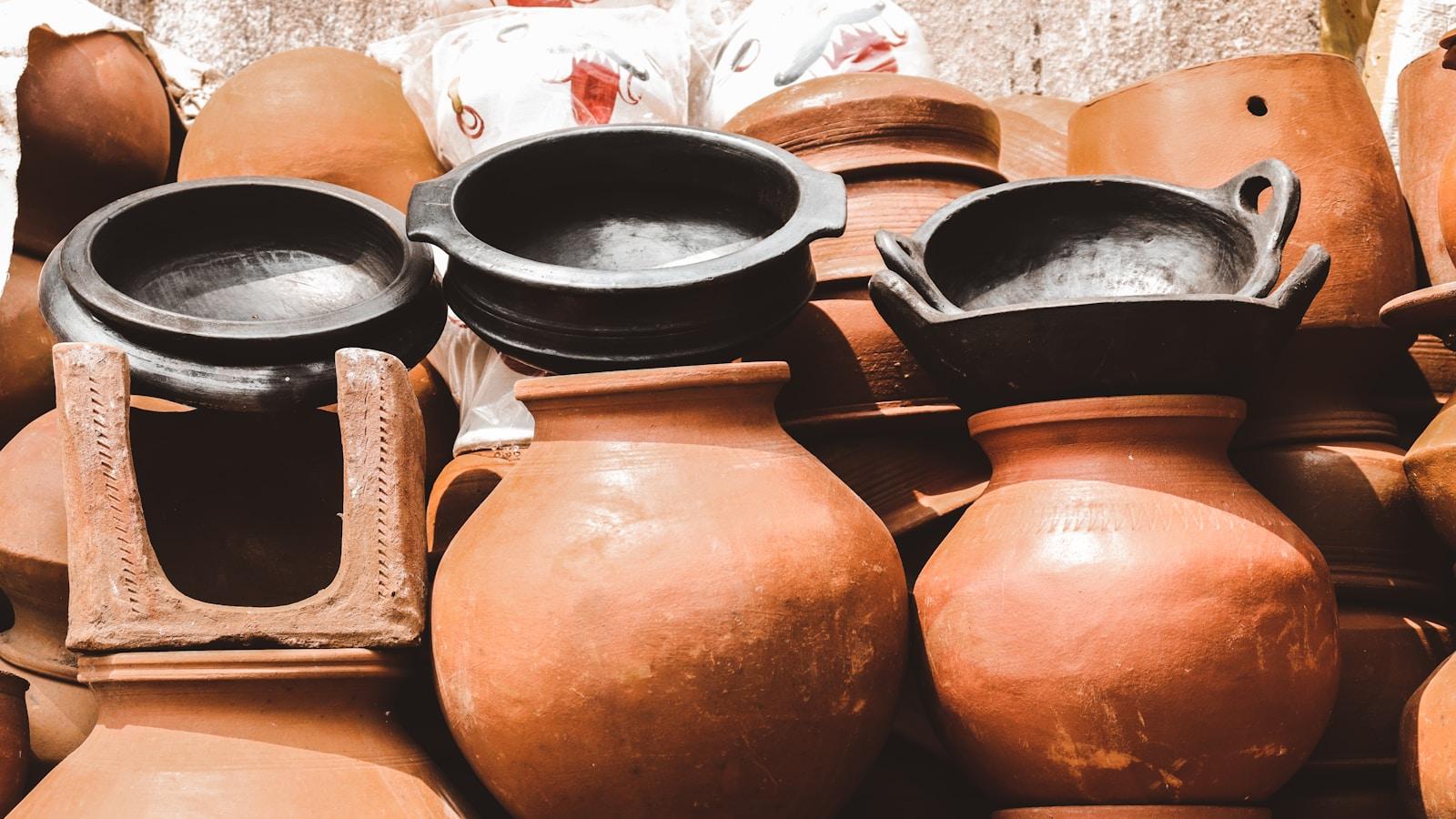 Potes e panelas de barro empilhados, em tons de terracota e preto