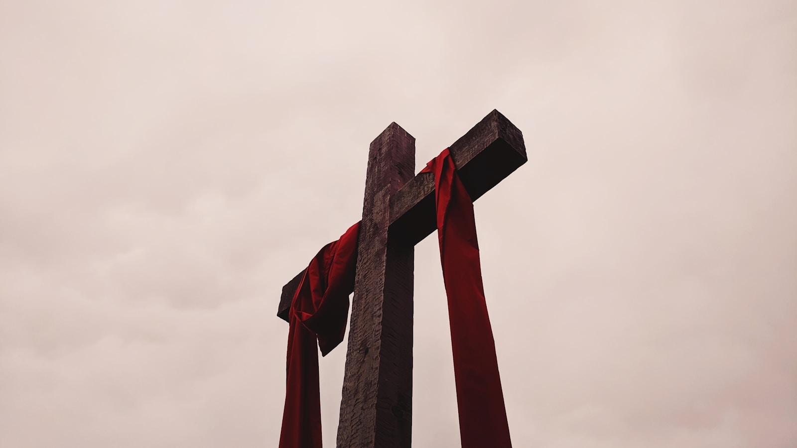 Cruz de pedra envolta em um pano vermelho, contra o céu nublado