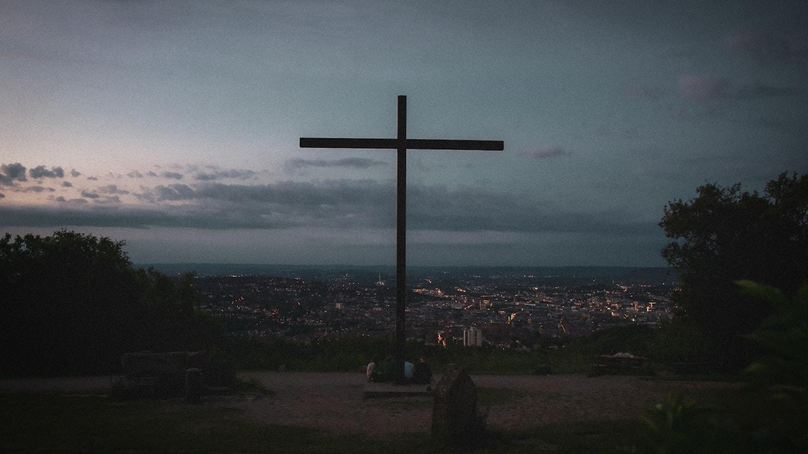 Grande cruz no alto de um mirante, com as luzes da cidade ao fundo no anoitecer