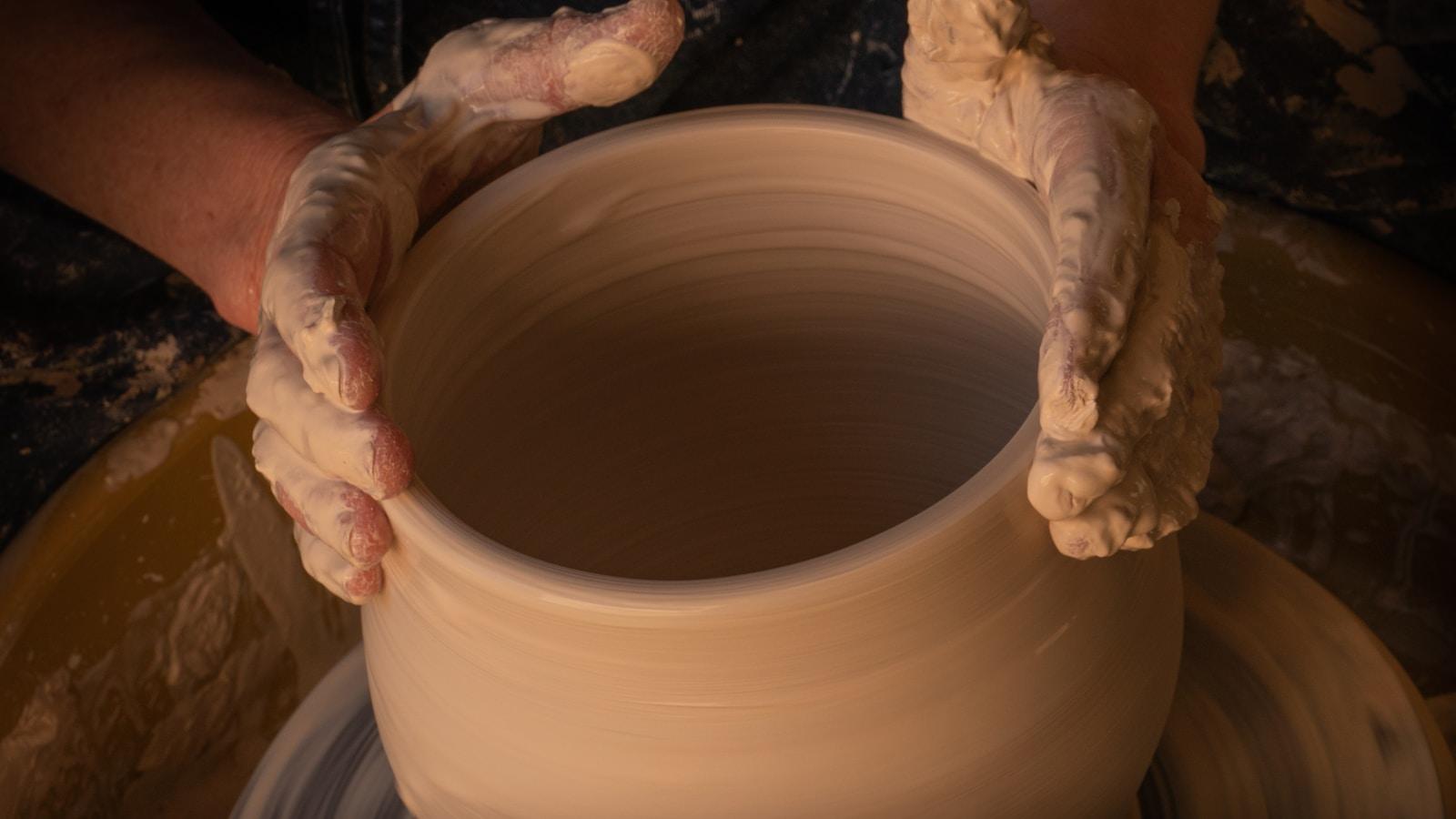 Mãos de um oleiro moldando um vaso de argila no torno