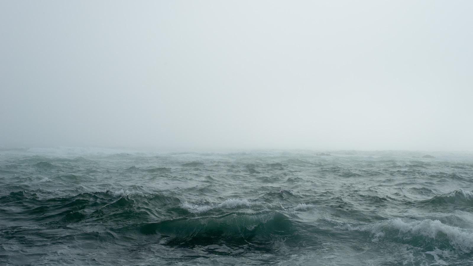 Mar agitado com ondas escuras sob névoa e céu cinza