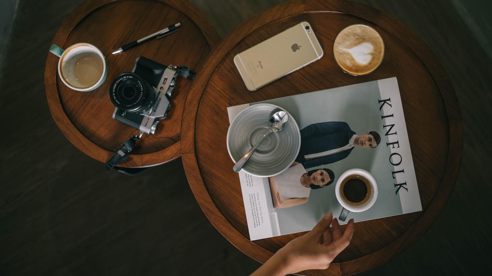 Mesa redonda de madeira com xícaras de café, uma revista e uma câmera fotográfica