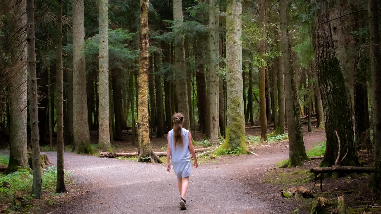 Mulher caminhando numa trilha de floresta que se bifurca em dois caminhos