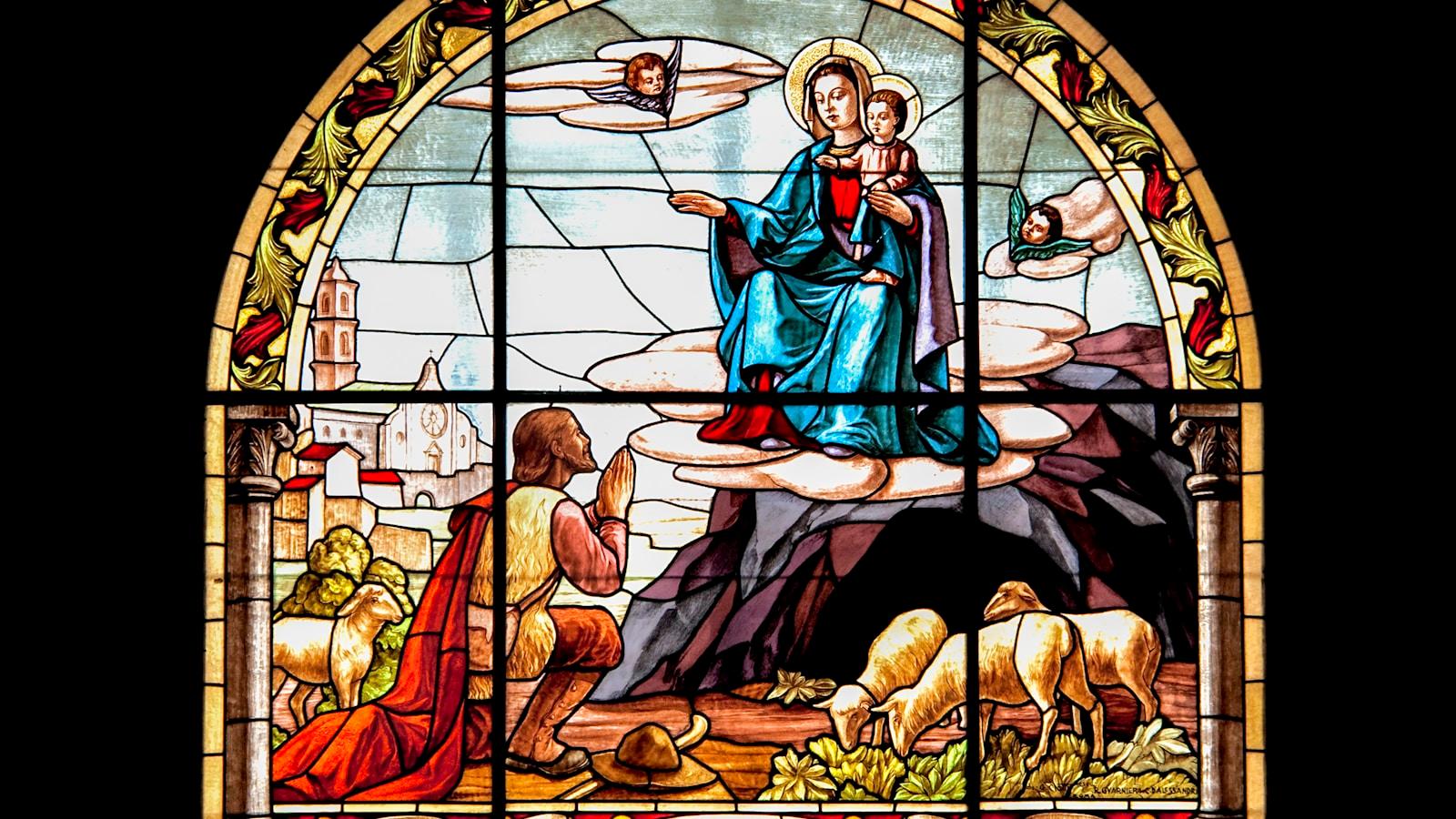 Vitral de Nossa Senhora com o Menino aparecendo a um pastor ajoelhado entre ovelhas