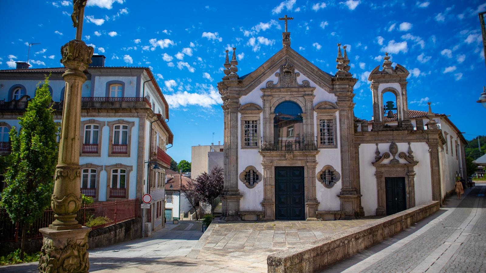 Igreja barroca de fachada branca e granito numa praça de vila portuguesa, sob céu azul