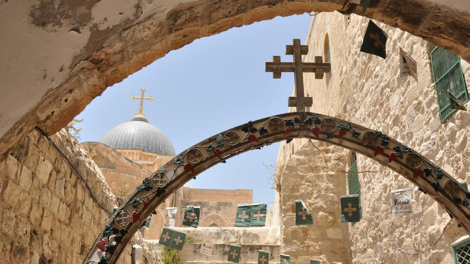 Rua de pedra em Jerusalém, com a cúpula do Santo Sepulcro e cruzes ao fundo