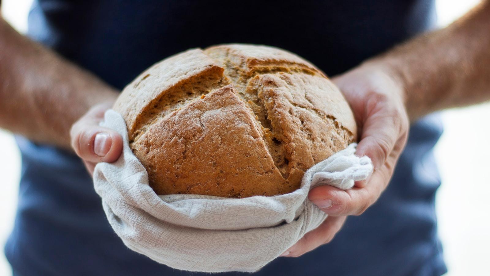 Mãos segurando um pão redondo envolto em pano branco