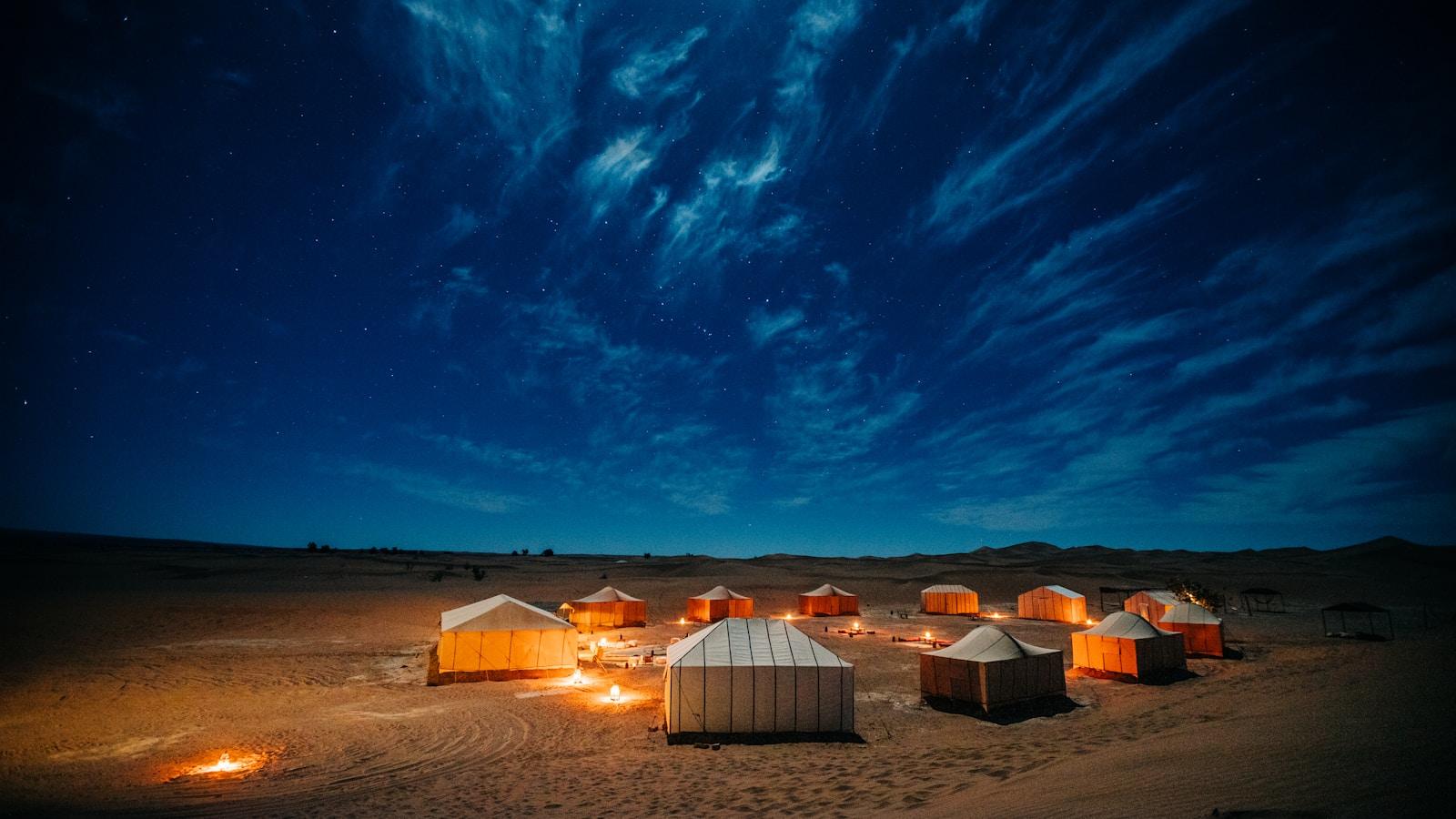 Acampamento de tendas iluminadas no deserto sob um céu estrelado