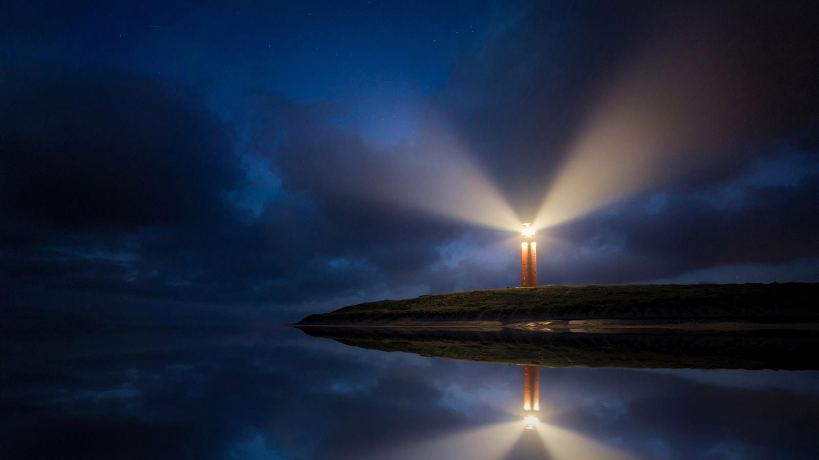 Farol aceso à noite, com feixes de luz refletidos na água