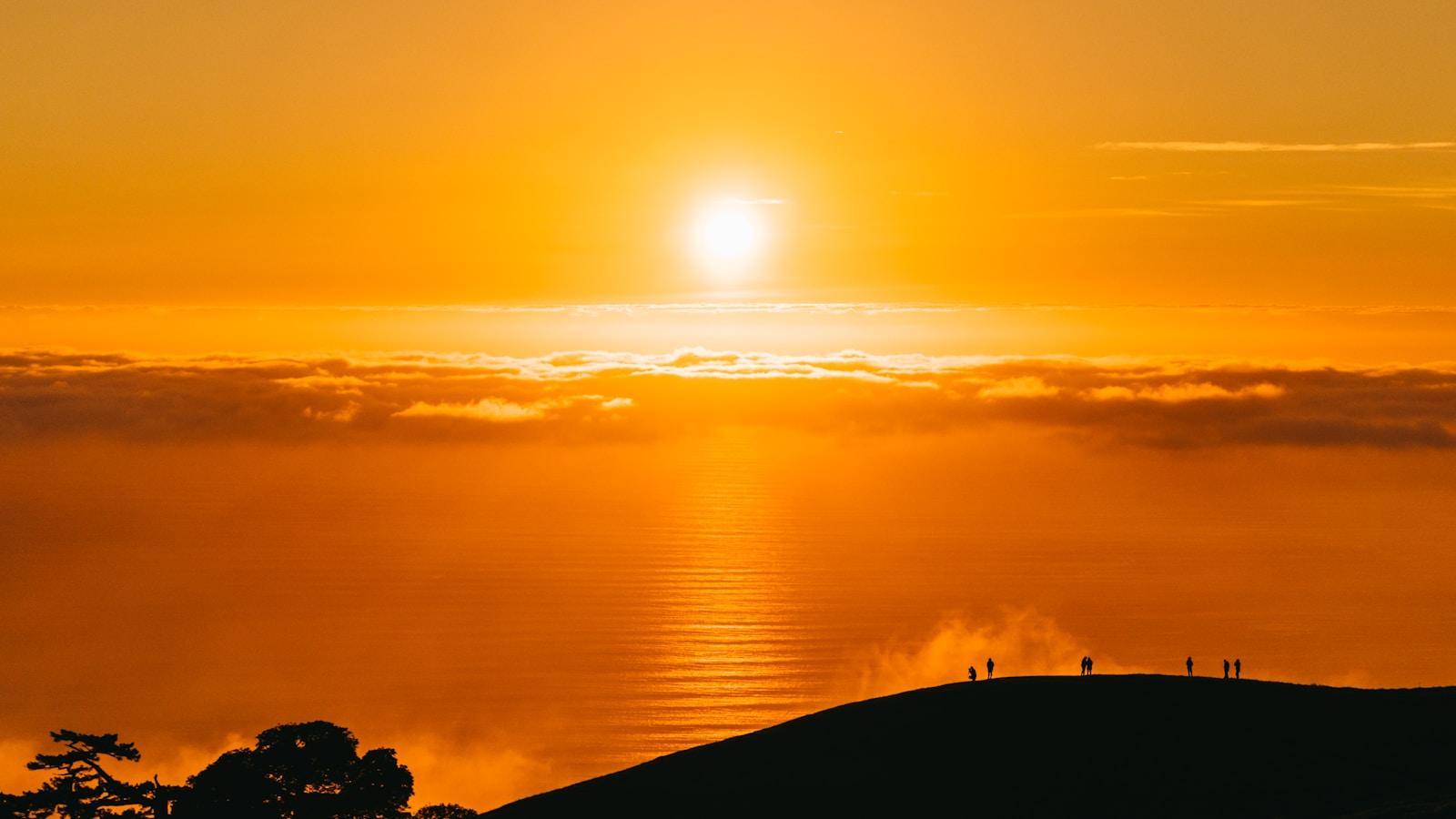 Sol nascendo sobre um mar de nuvens, com silhuetas de pessoas numa colina