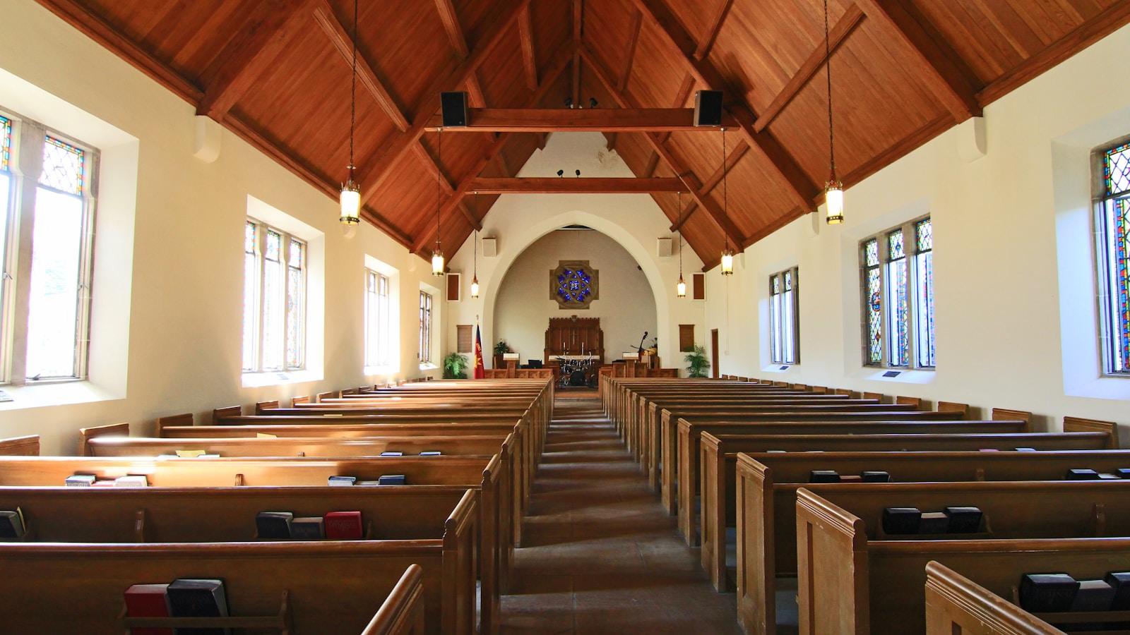Interior de uma igreja com bancos de madeira e teto de vigas, visto do fundo da nave