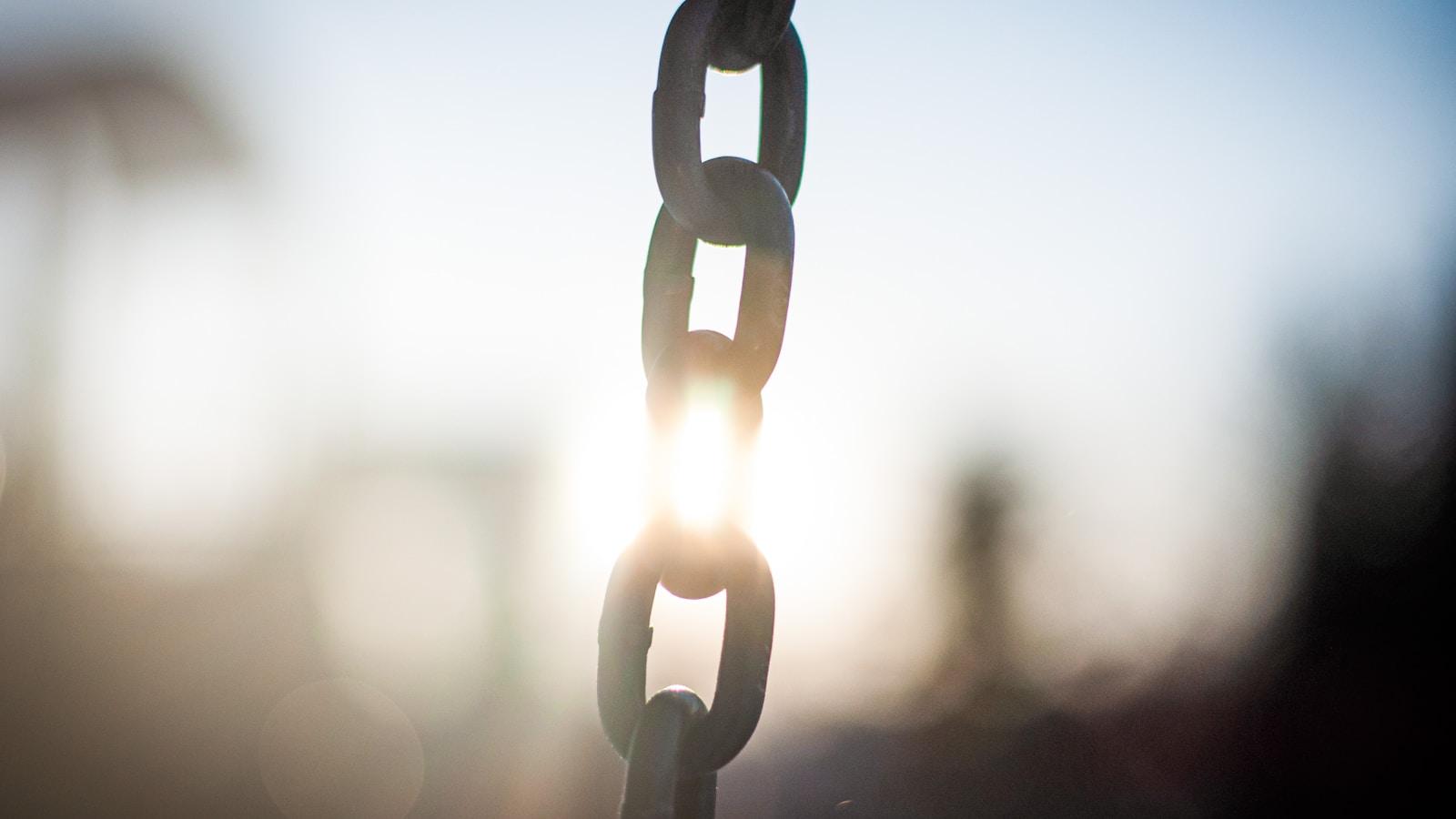 Elos de uma corrente de metal contra o sol, em contraluz