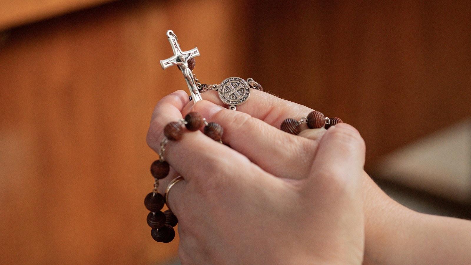 Mãos juntas segurando um rosário de contas de madeira com crucifixo de metal