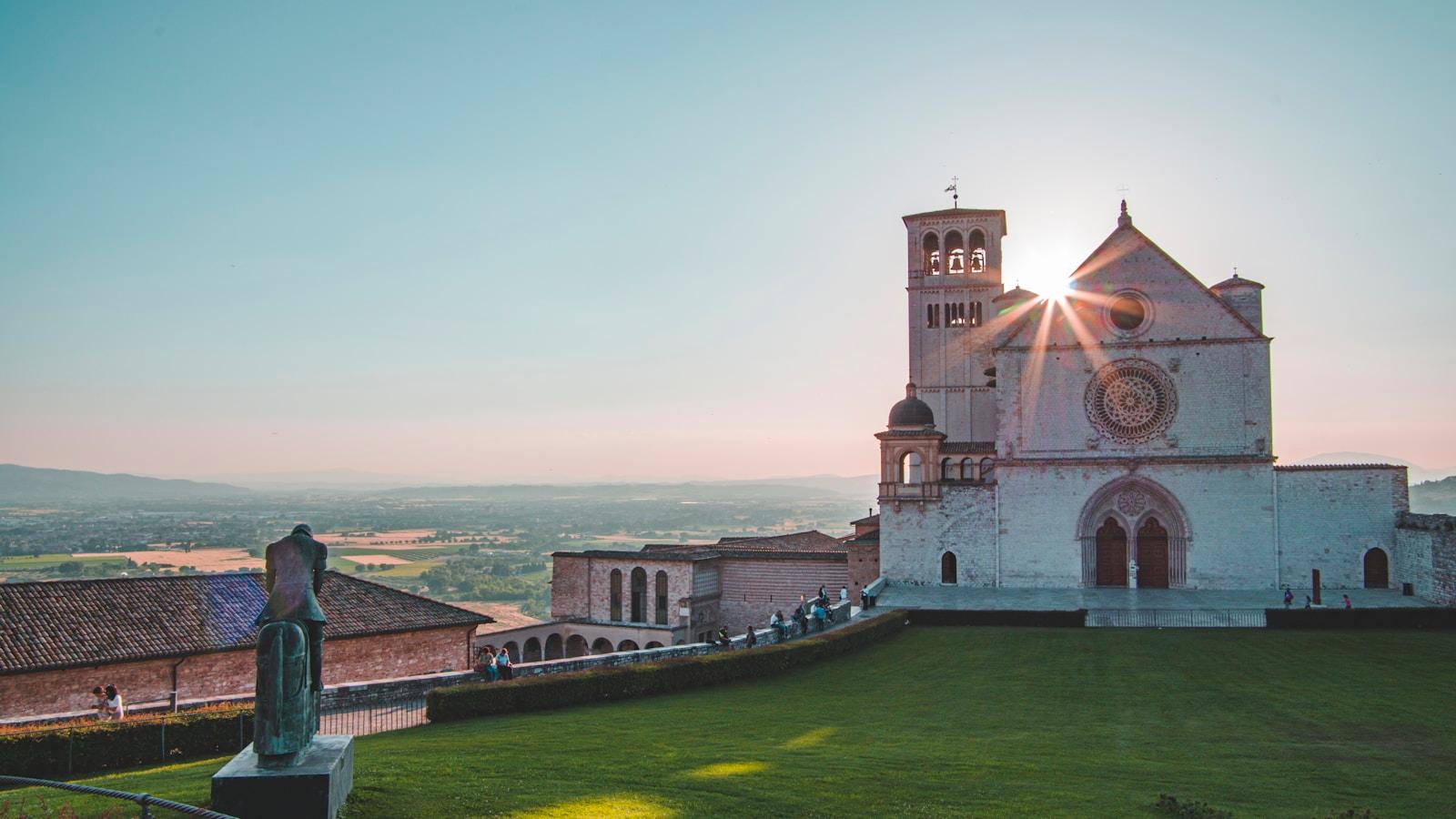 Basílica de São Francisco, em Assis, com o sol atrás da torre e a planície ao fundo