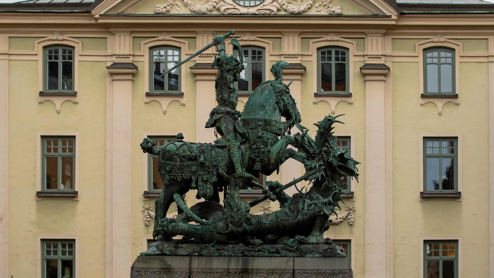 Estátua de bronze de São Jorge a cavalo matando o dragão, diante de um prédio