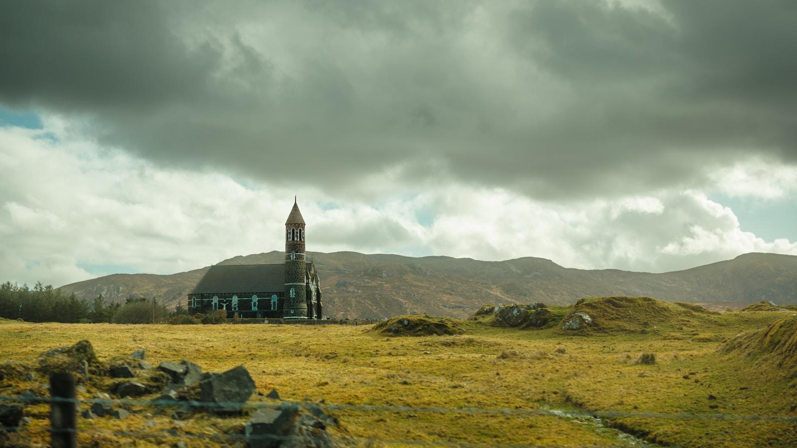 Igreja de pedra com torre numa paisagem de campos e montes na Irlanda, sob nuvens carregadas