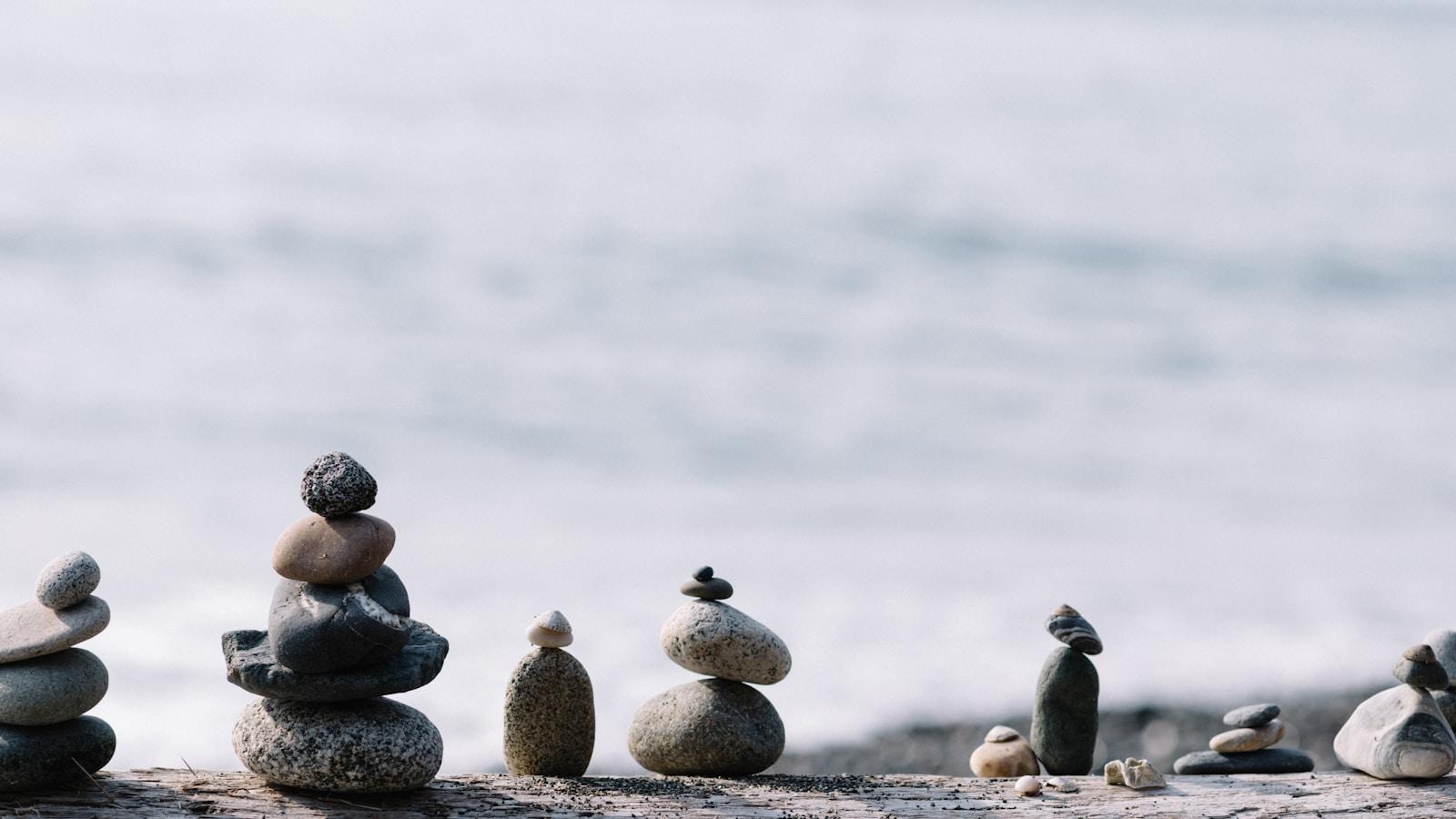 Pequenas pilhas de pedras equilibradas sobre uma prancha, com o mar desfocado ao fundo