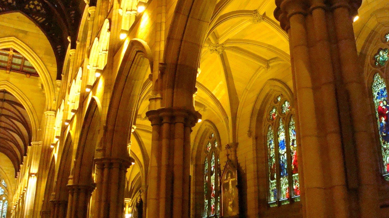 Nave gótica iluminada, com arcos de pedra e vitrais ao fundo