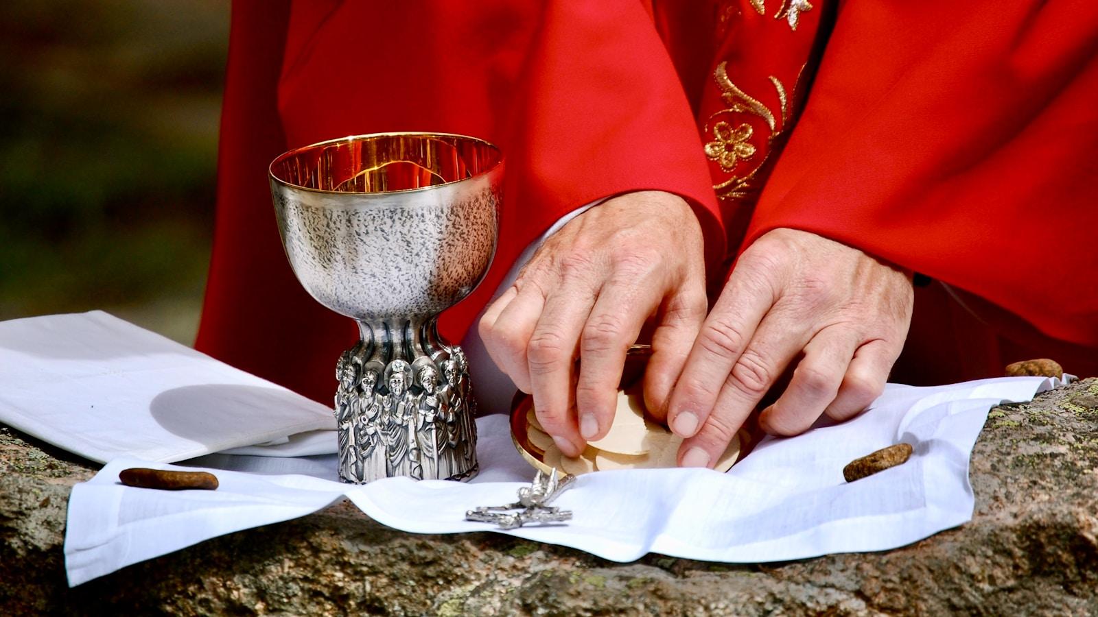 Sacerdote de casula vermelha segurando a hóstia sobre o cálice, em close das mãos