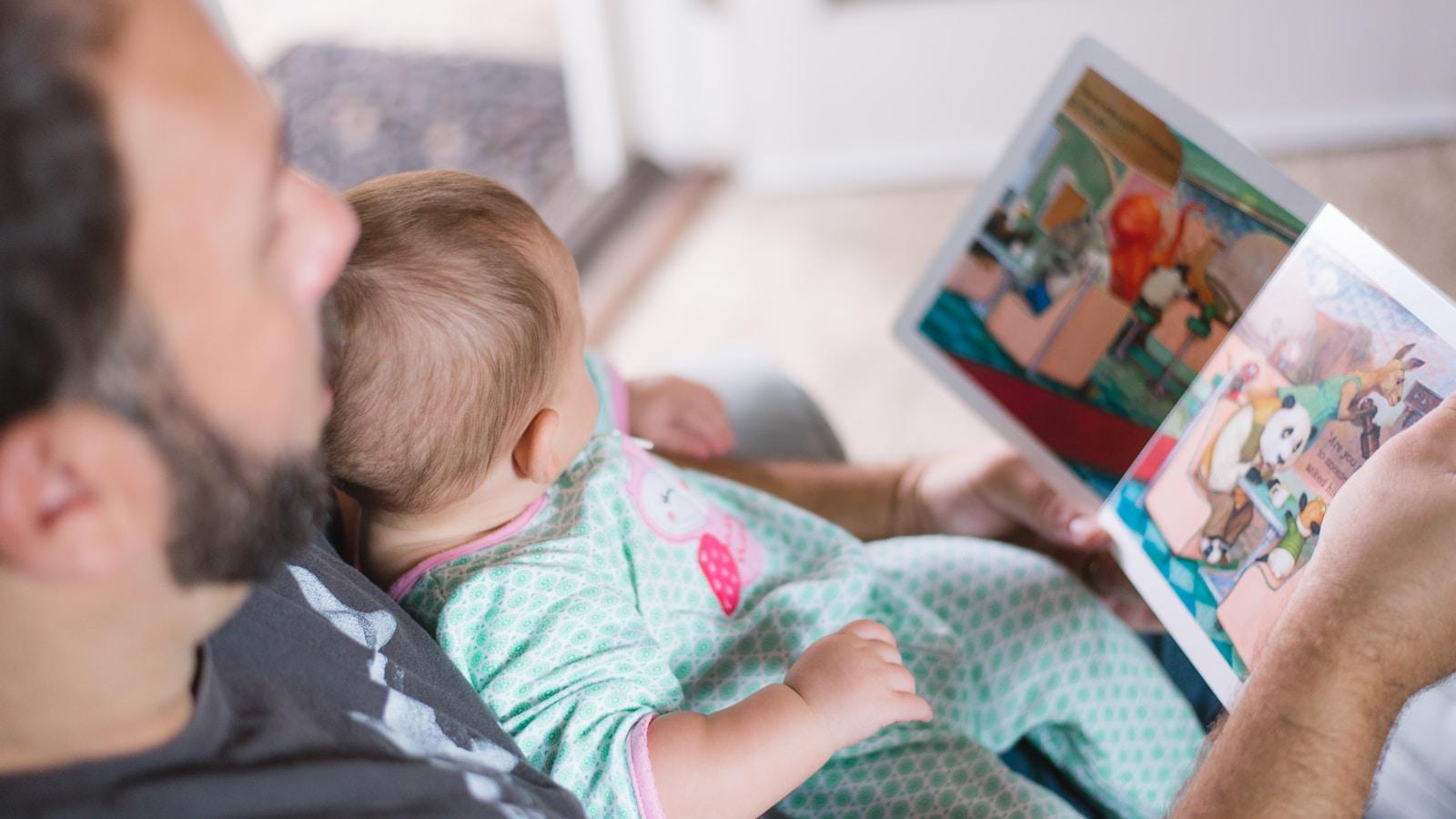 Pai lendo um livro ilustrado com o bebê no colo