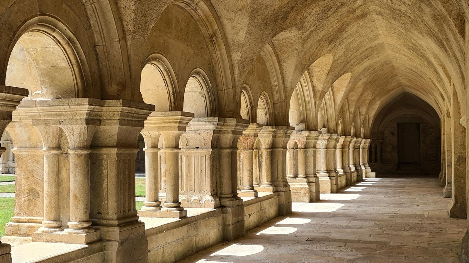 Claustro românico da Abadia de Fontenay, com arcos de pedra e luz do sol