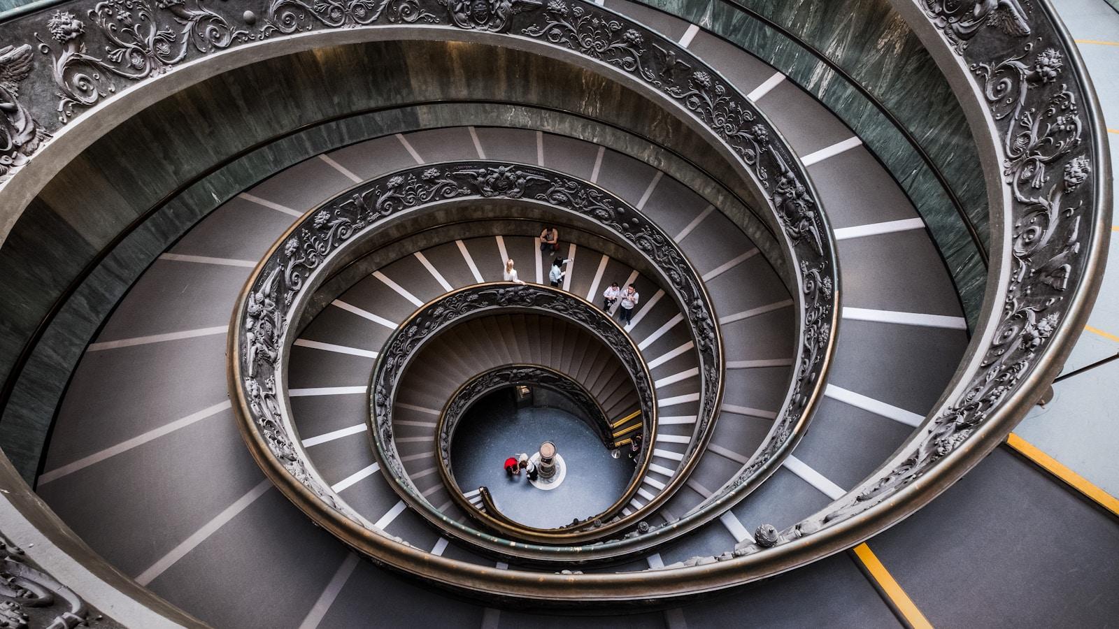 Escada em espiral dos Museus do Vaticano vista de cima, com pessoas subindo pelas voltas