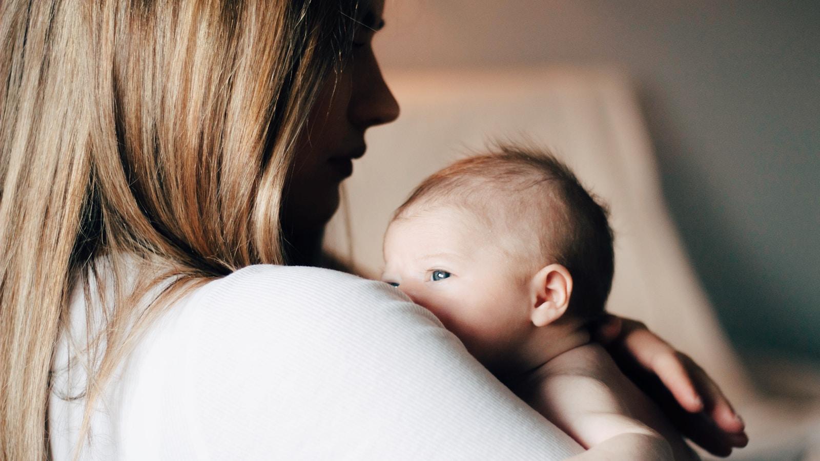 Mãe segurando um bebê recém-nascido no colo, junto ao ombro
