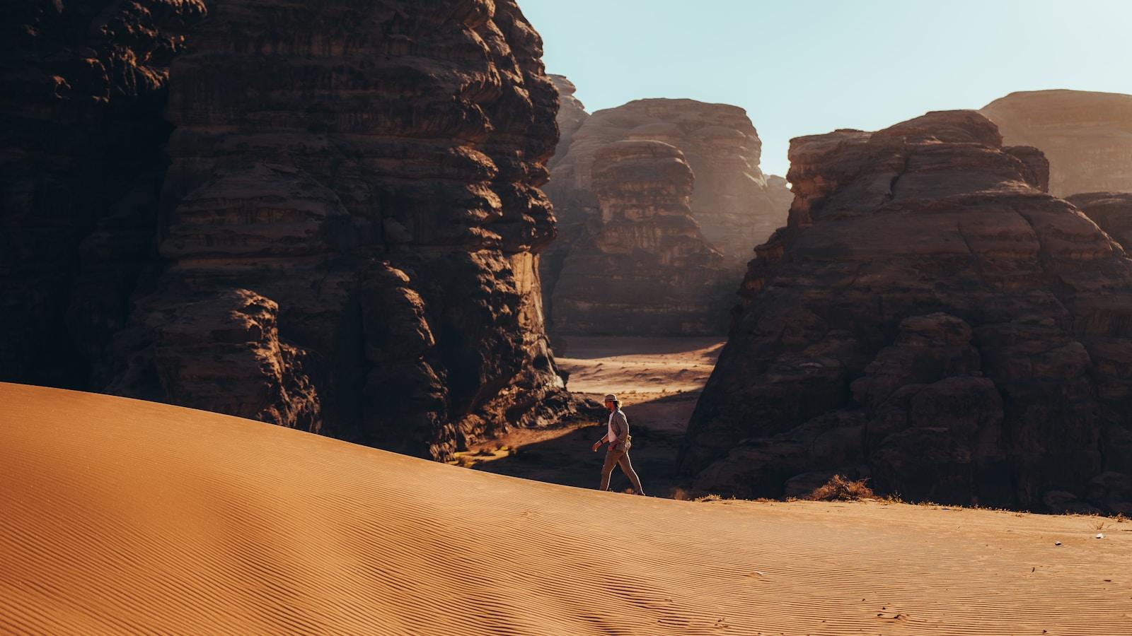 Pessoa caminhando sozinha entre rochas e dunas de areia no deserto