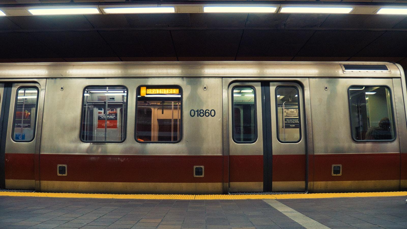 Vagão de metrô prateado com faixa vermelha parado na estação