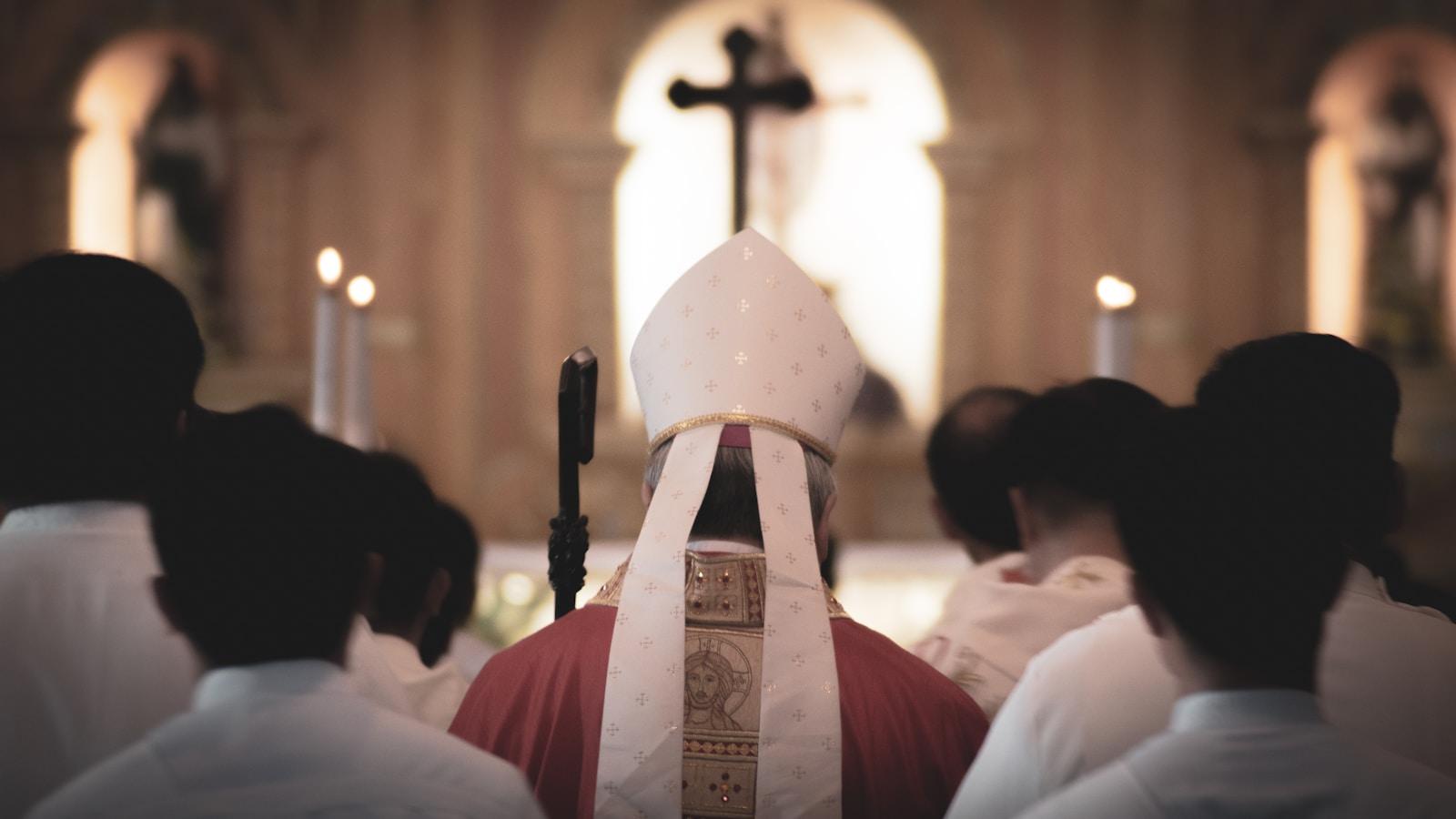 Bispo com mitra e casula vermelha diante do altar, visto por trás dos fiéis