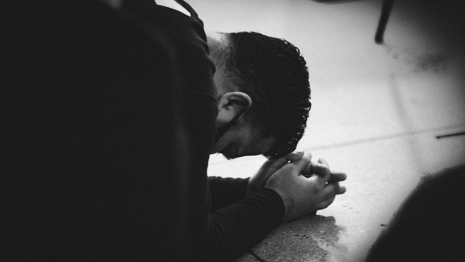 Homem de cabeça baixa apoiada nas mãos, em oração, em preto e branco