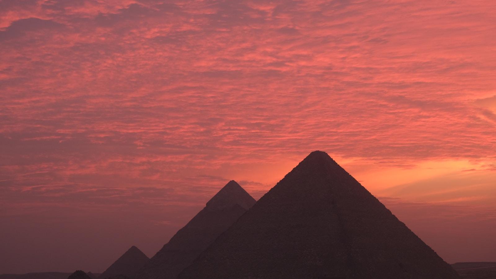 Pirâmides de Gizé em silhueta contra um céu avermelhado ao pôr do sol