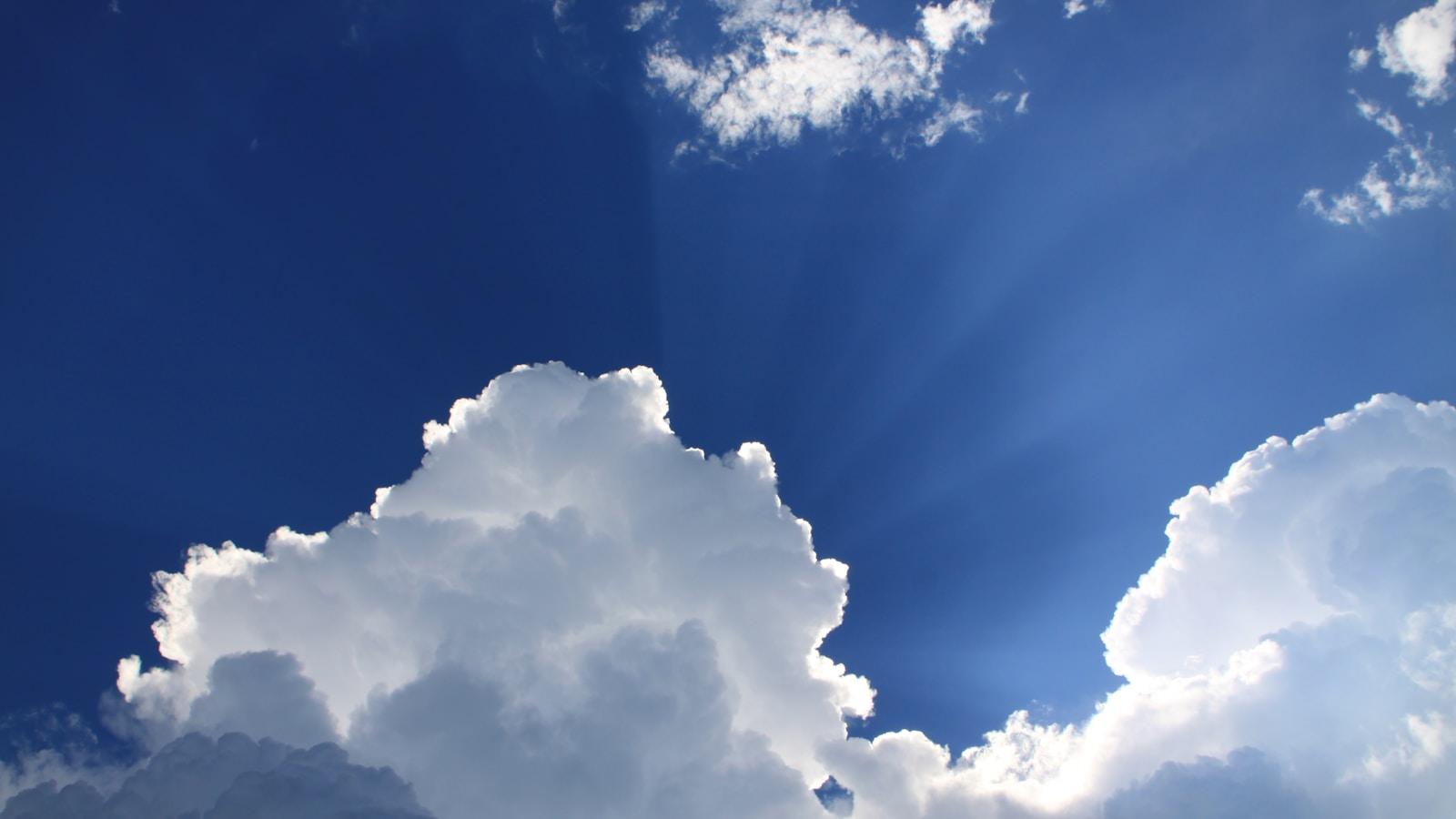 Nuvens brancas com raios de sol contra um céu azul intenso