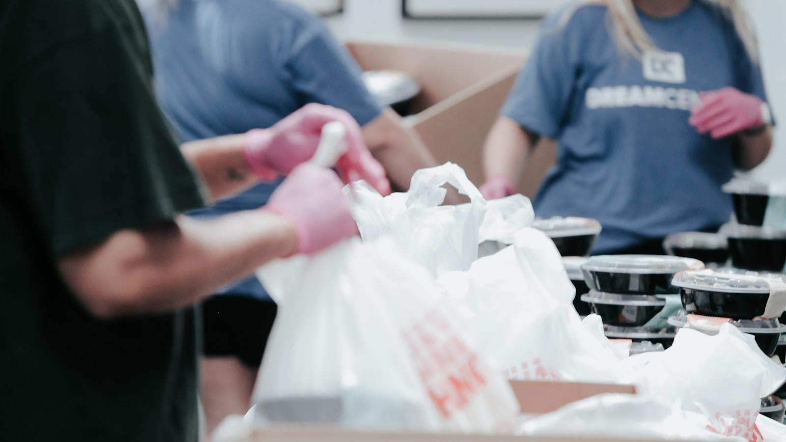 Voluntários com luvas embalando refeições em sacolas para doação