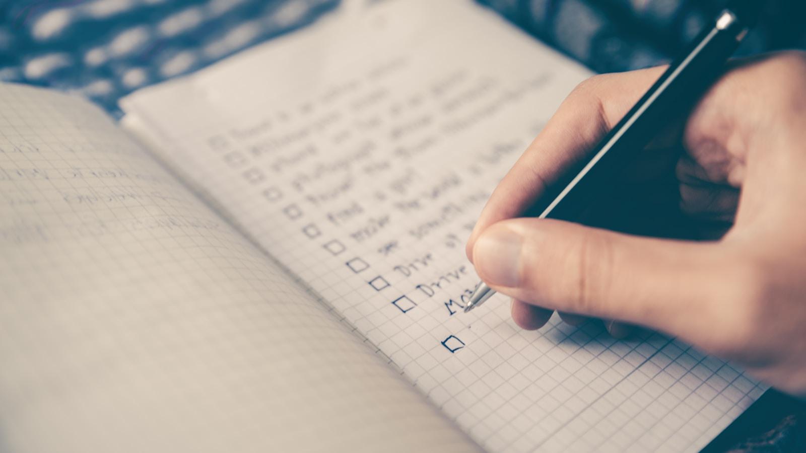Mão escrevendo uma lista de tarefas com caixas de marcação num caderno