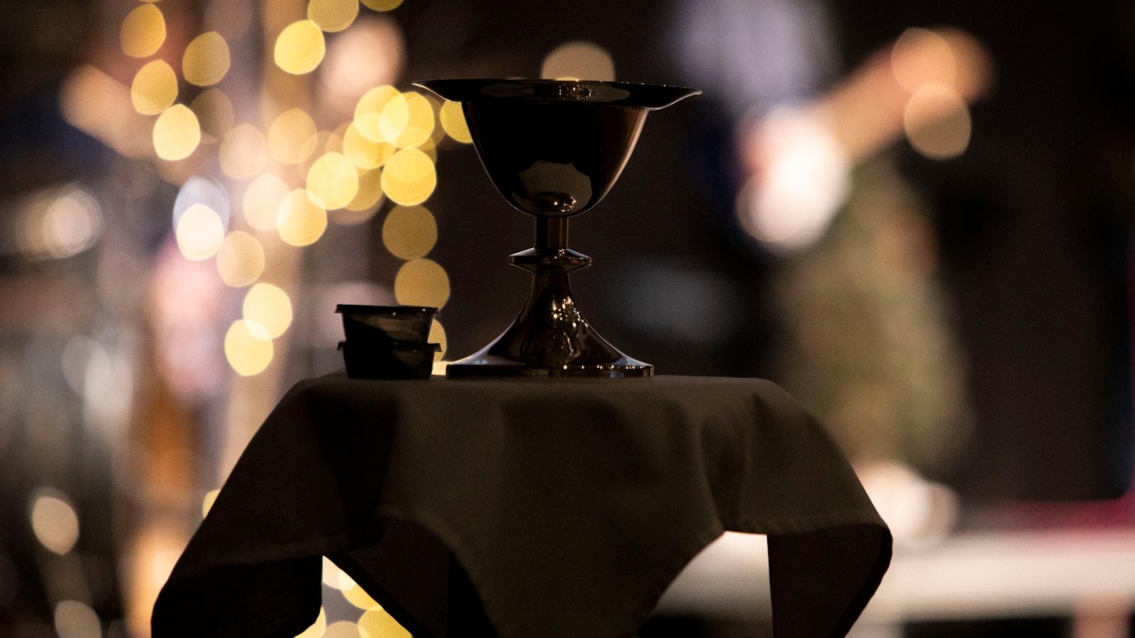 Cálice escuro sobre uma mesa coberta de pano preto, com luzes desfocadas ao fundo