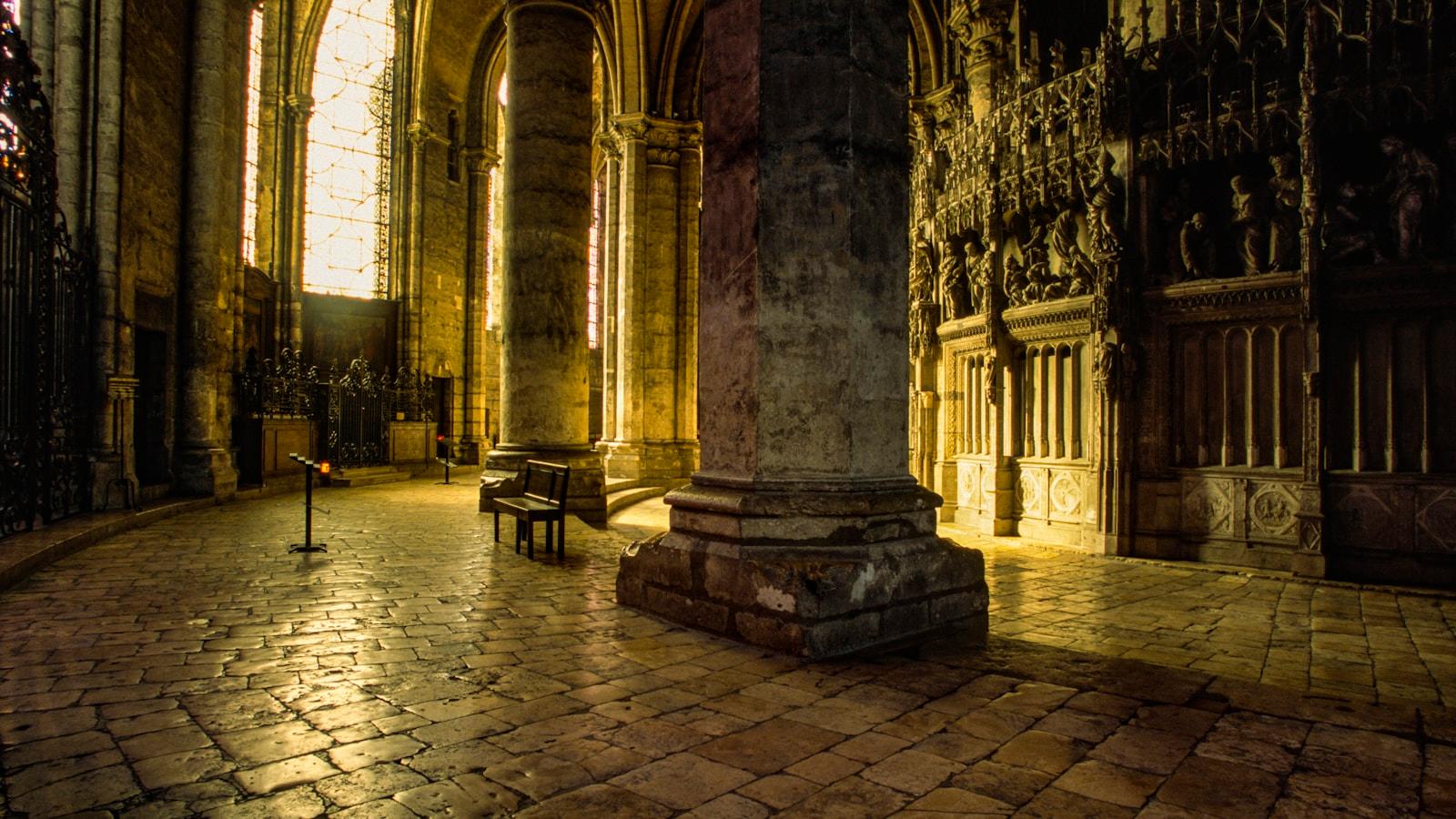 Interior de catedral medieval com colunas de pedra e piso iluminado pela luz das janelas