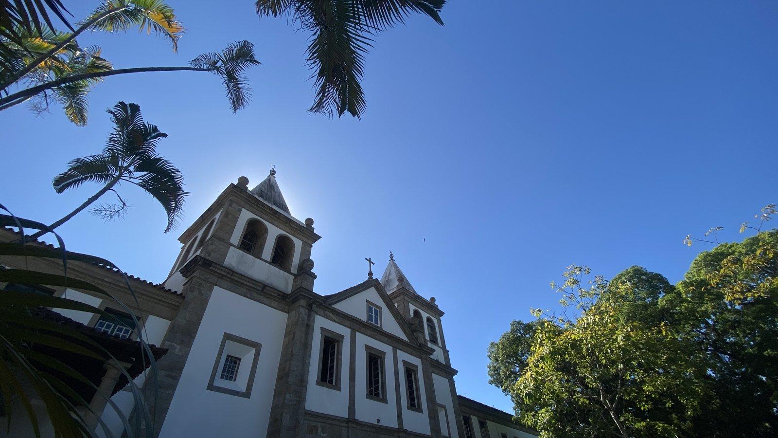 Fachada de igreja colonial de estilo beneditino, entre árvores