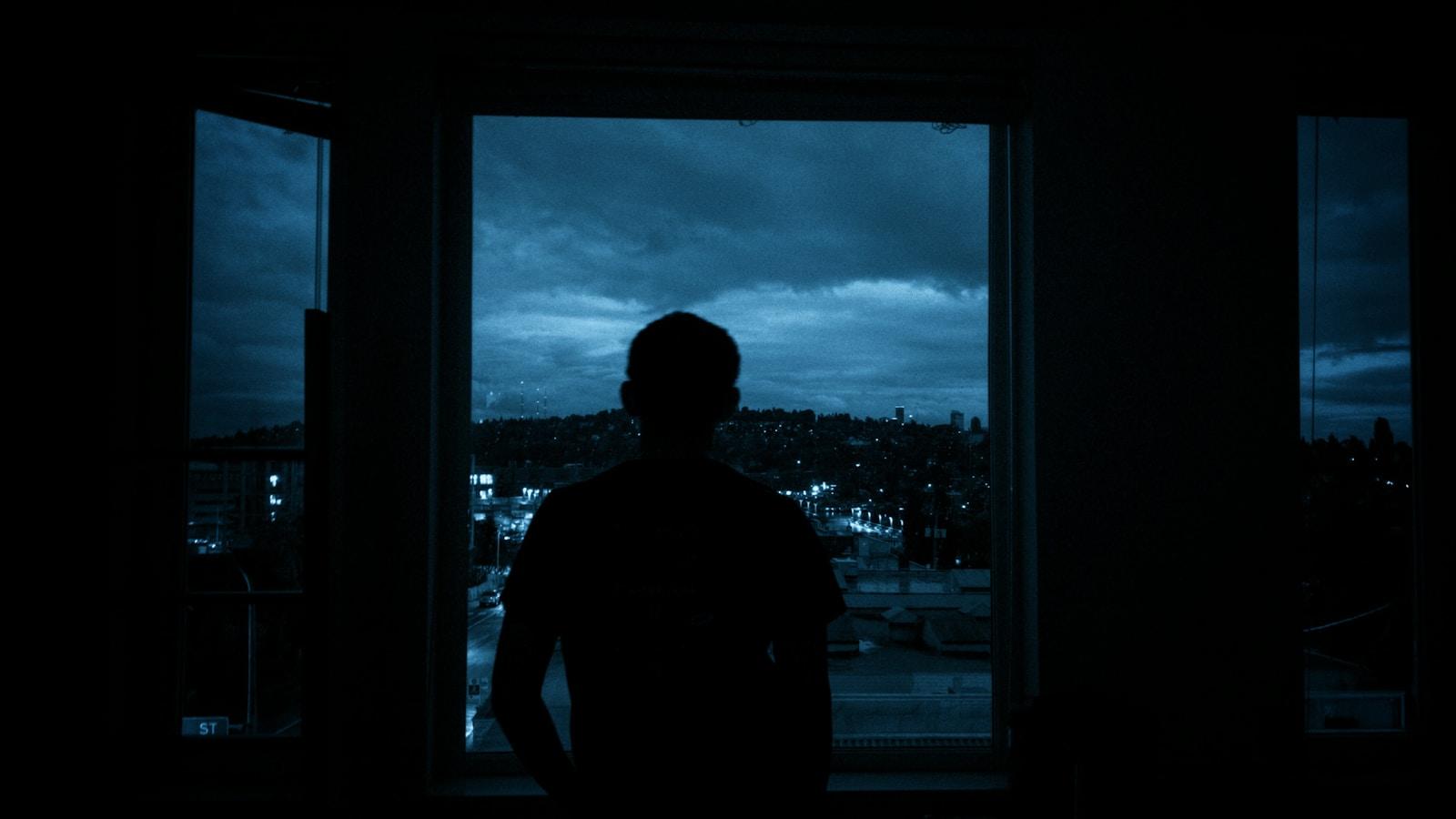 Silhueta de um homem diante de uma janela, olhando a cidade à noite