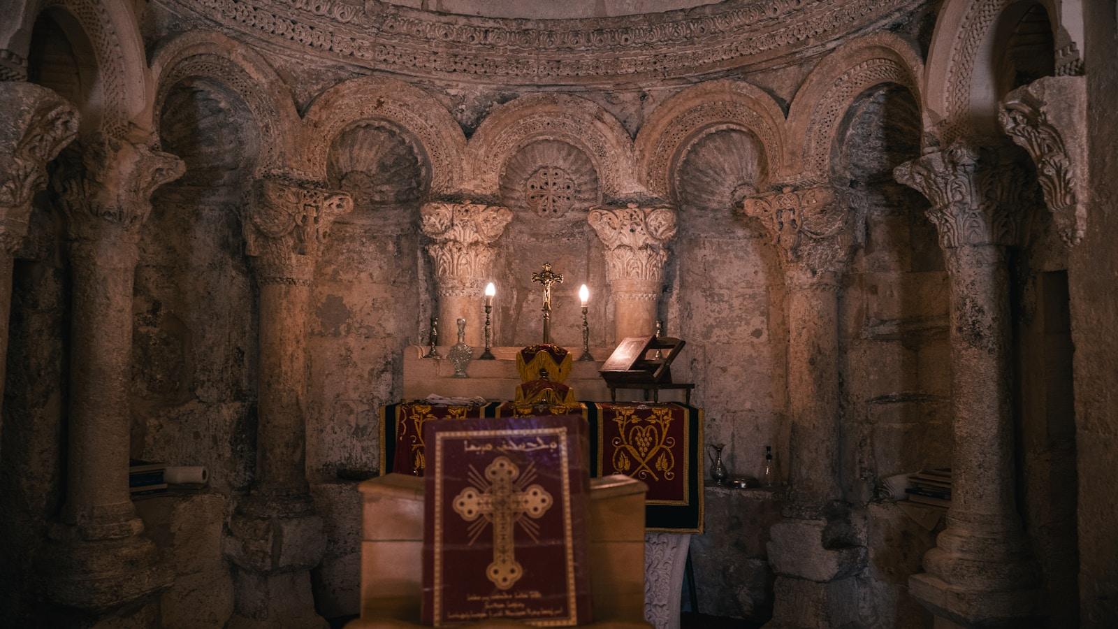 Interior de uma igreja antiga de pedra, com altar, crucifixo e duas velas acesas entre colunas