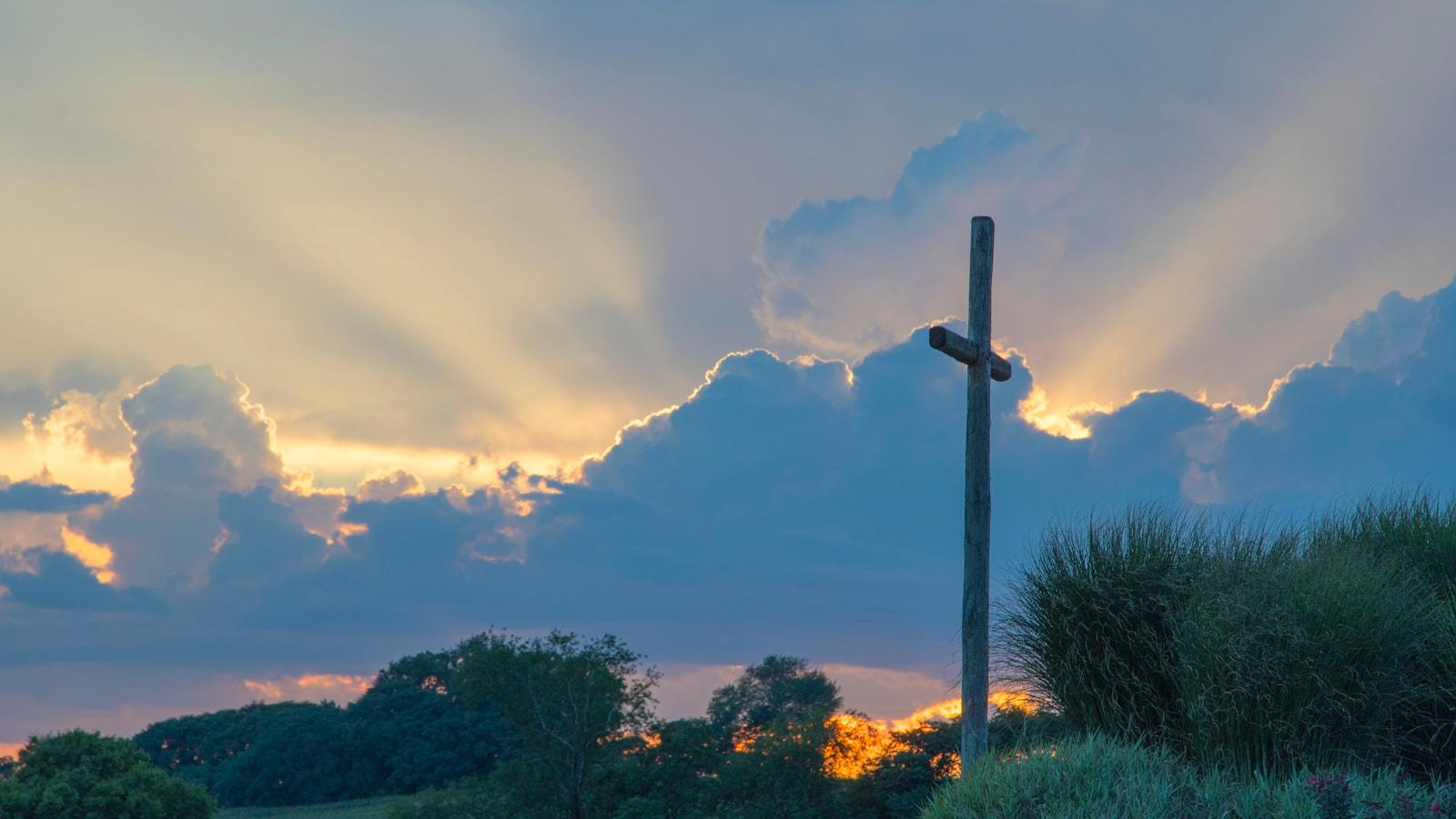 Cruz de madeira contra um céu de nuvens atravessado por raios de sol