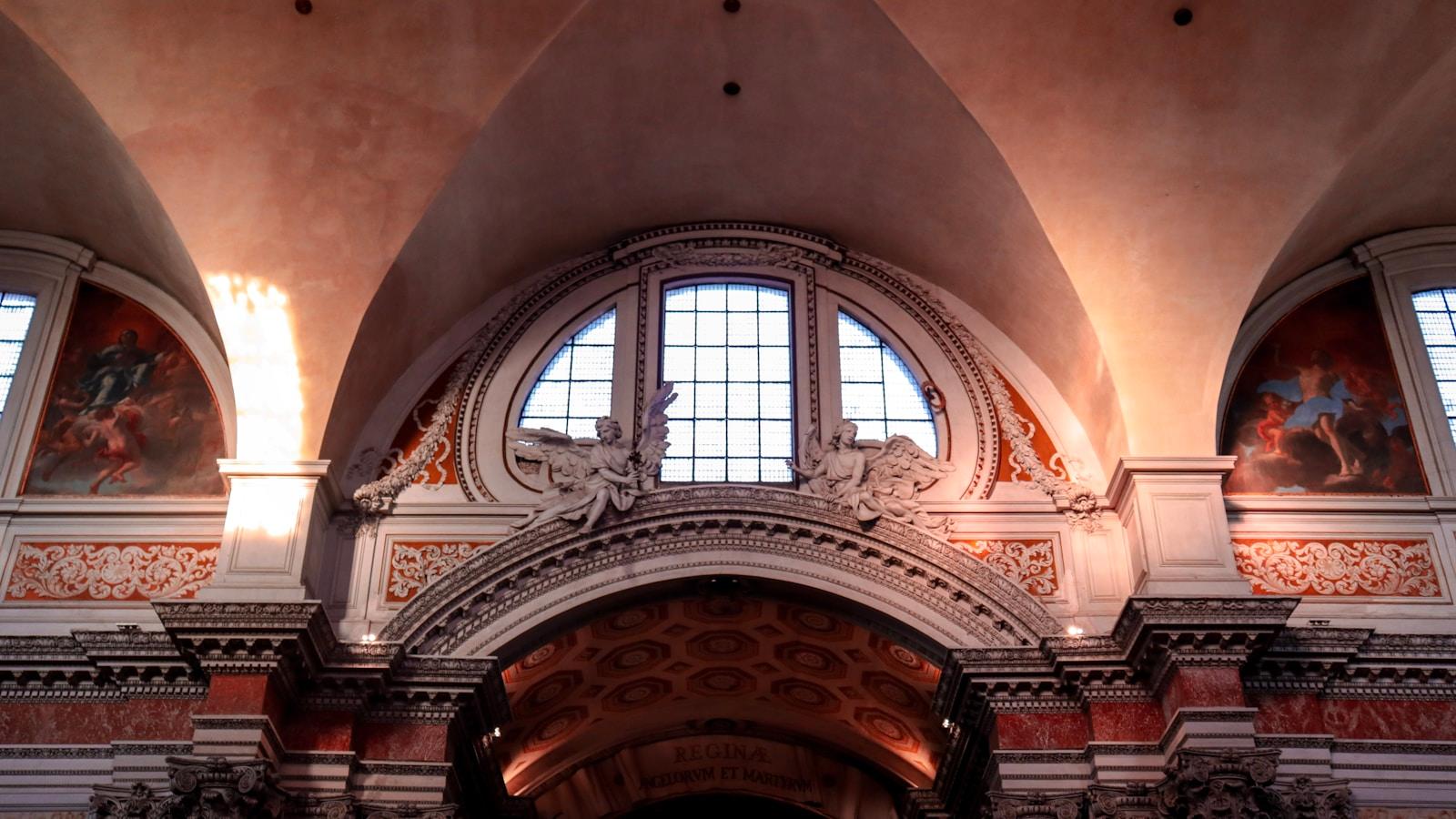 Interior de igreja barroca com arco decorado, janela alta e afrescos nas paredes