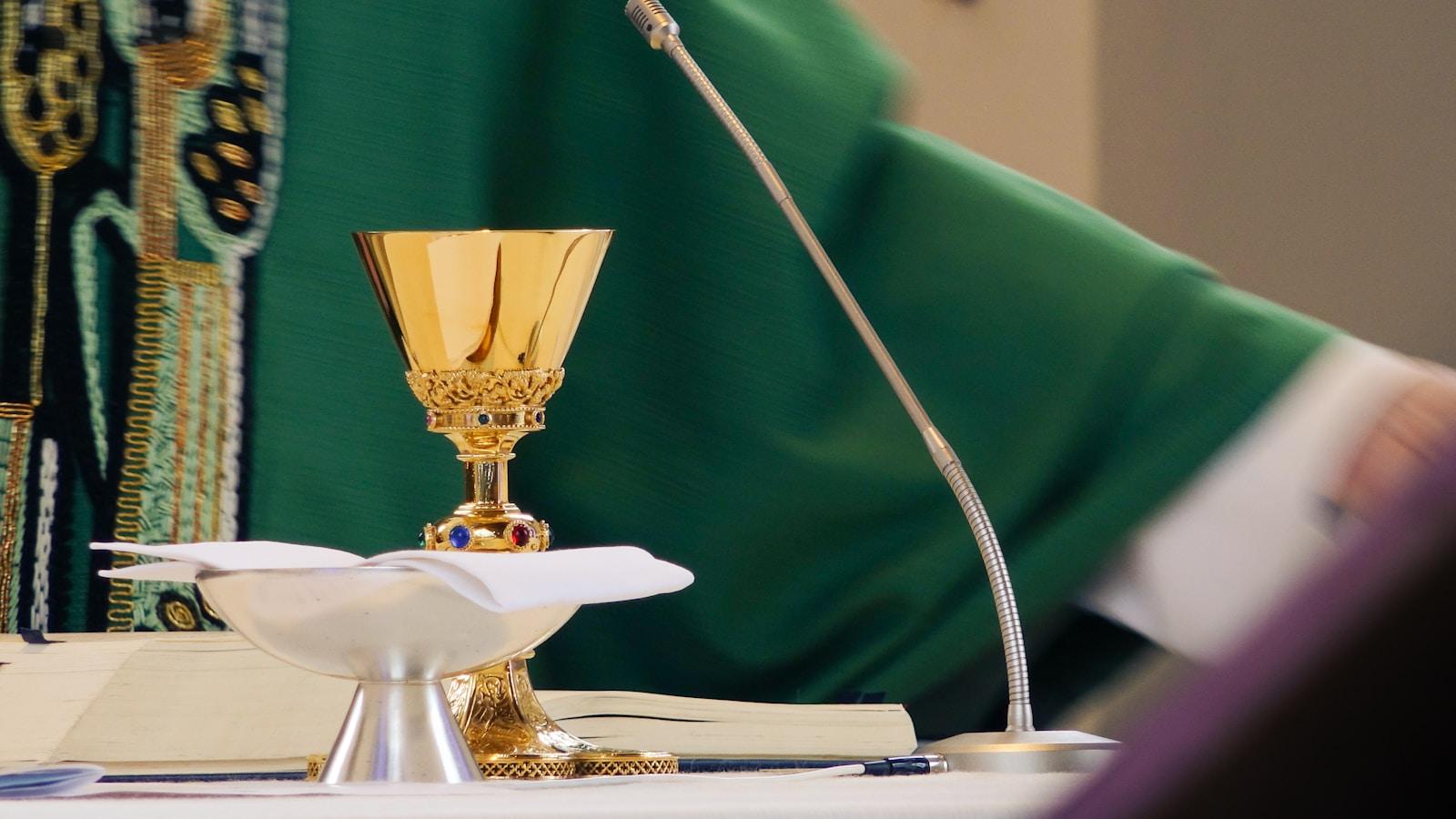 Cálice dourado e pátena com hóstia sobre o altar, diante de um sacerdote com paramento verde